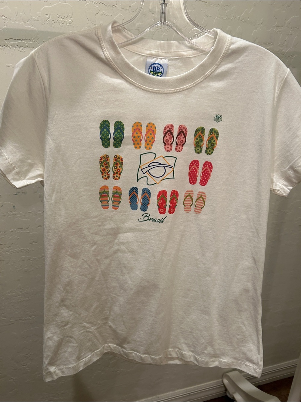 White crew neck t-shirt with colorful flip-flop graphic and “Brasil” script.